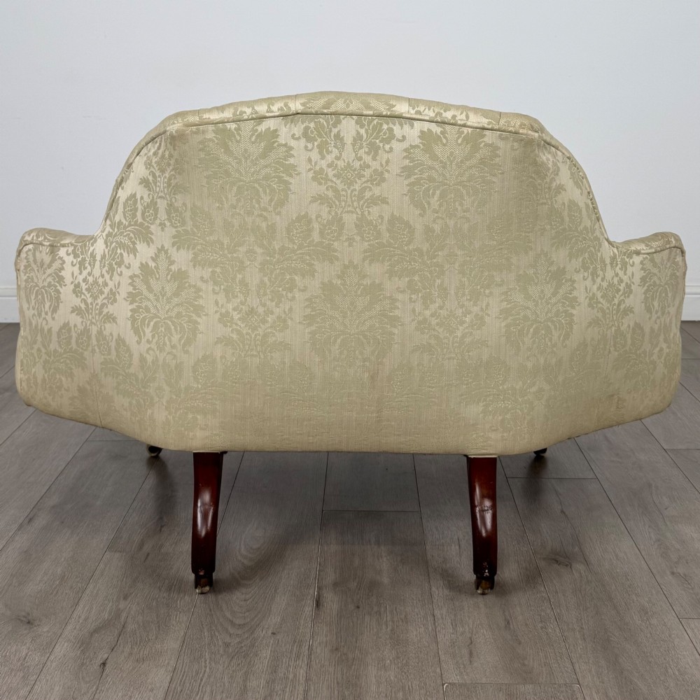 A 19th-century Victorian settee upholstered in sage green patterned damask with button-tufting and carved dark mahogany legs on ceramic castors. View V