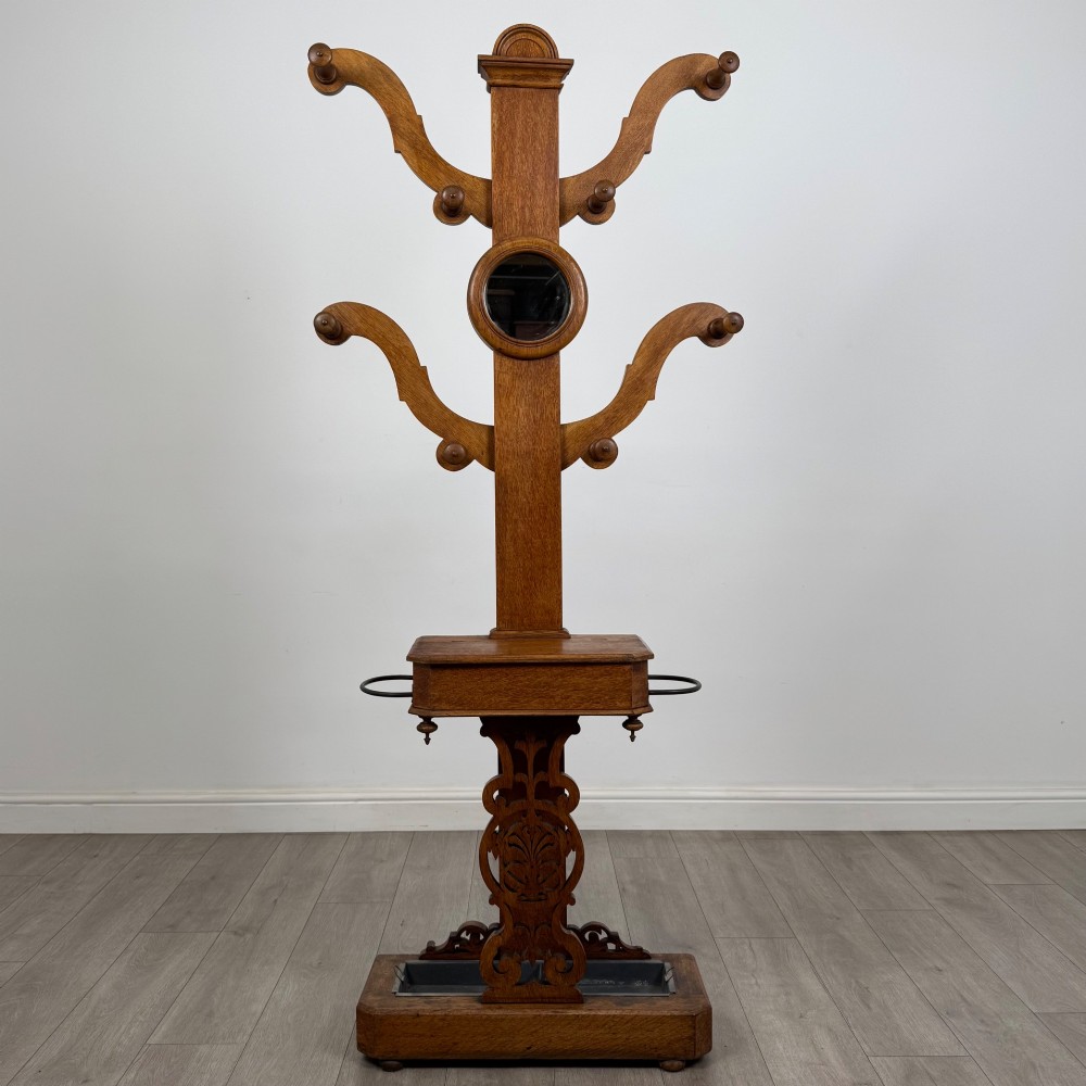 A nineteenth-century Victorian mahogany hall stand featuring coat pegs, a central circular mirror, metal umbrella loops, carved lower scrollwork, and a base drip tray.