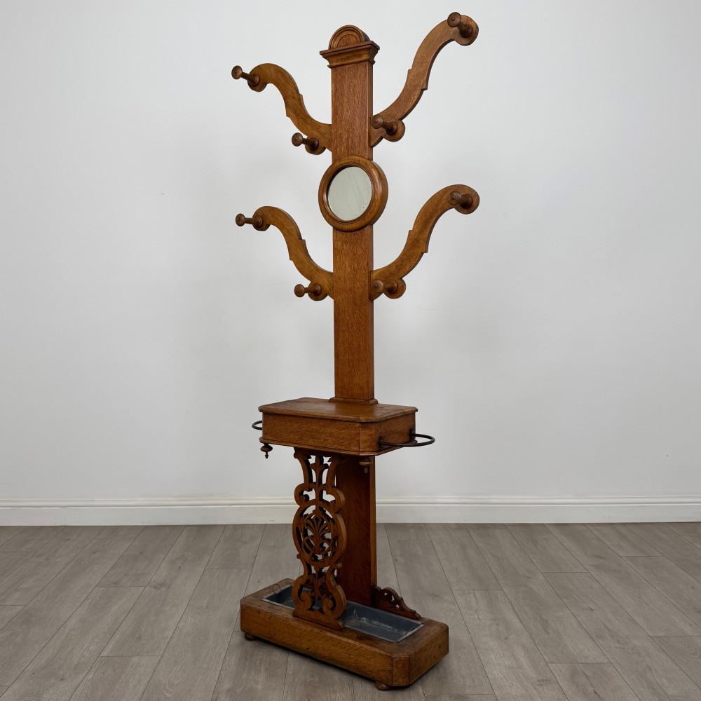A nineteenth-century Victorian mahogany hall stand featuring coat pegs, a central circular mirror, metal umbrella loops, carved lower scrollwork, and a base drip tray. View II