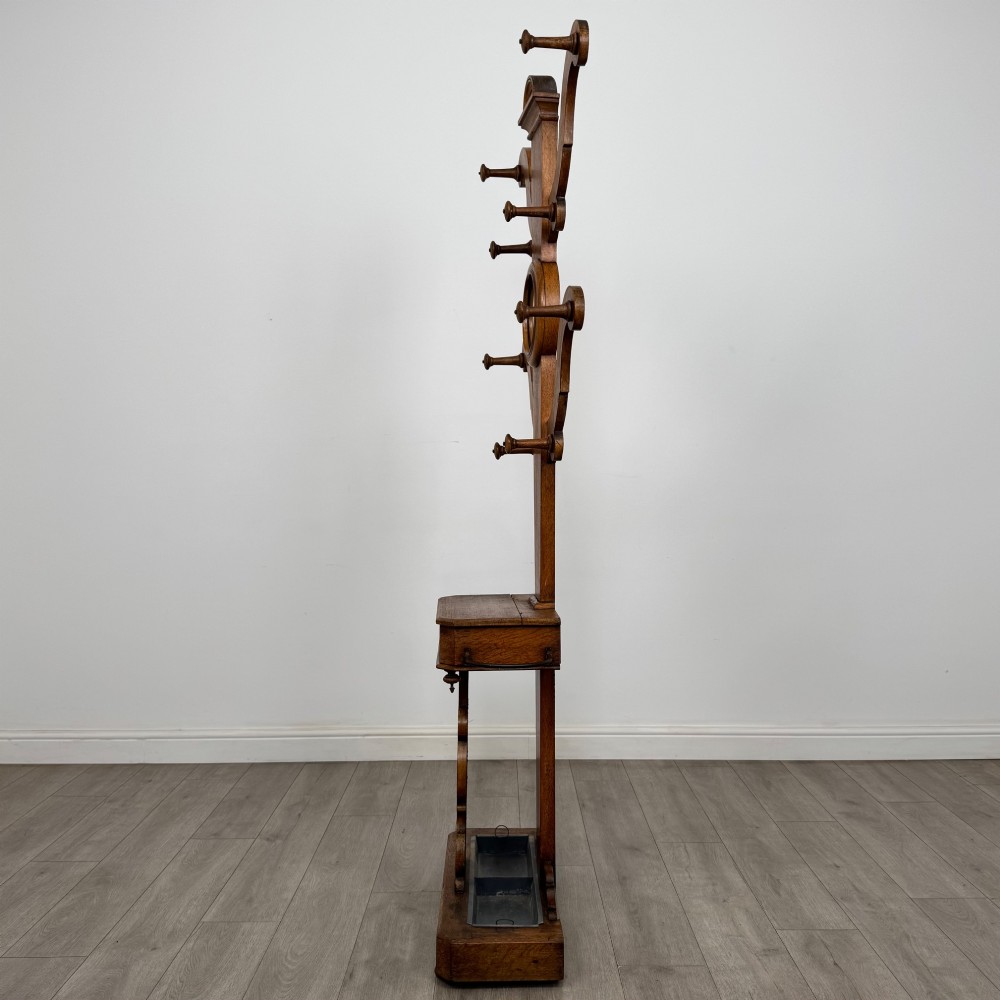 A nineteenth-century Victorian mahogany hall stand featuring coat pegs, a central circular mirror, metal umbrella loops, carved lower scrollwork, and a base drip tray. View III