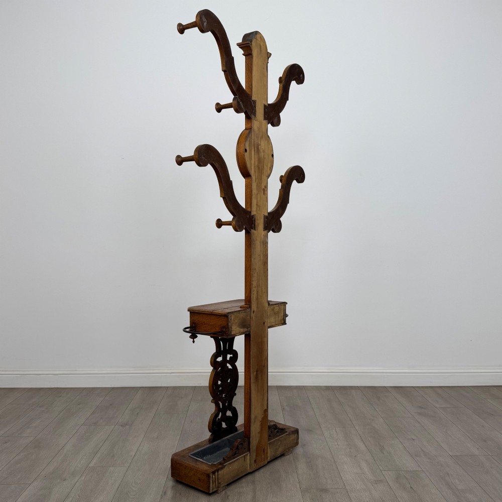 A nineteenth-century Victorian mahogany hall stand featuring coat pegs, a central circular mirror, metal umbrella loops, carved lower scrollwork, and a base drip tray. View IV