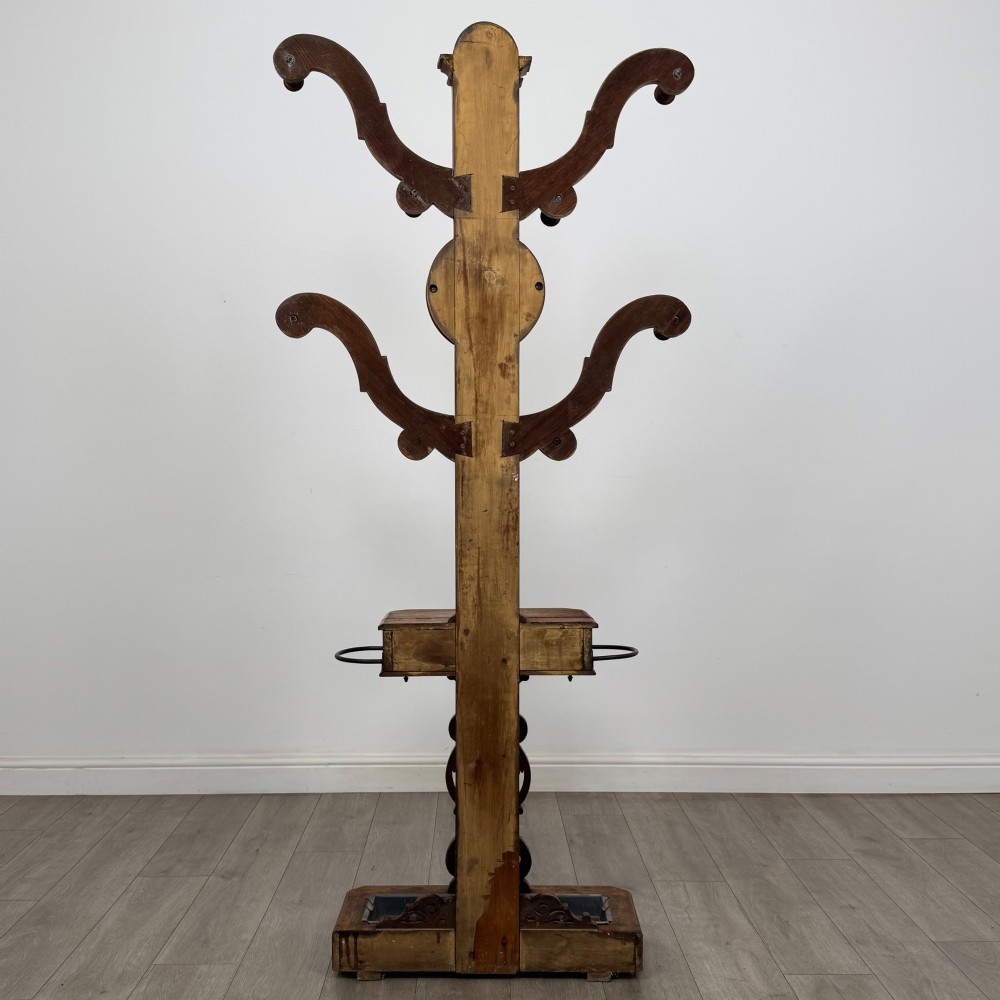 A nineteenth-century Victorian mahogany hall stand featuring coat pegs, a central circular mirror, metal umbrella loops, carved lower scrollwork, and a base drip tray. View V
