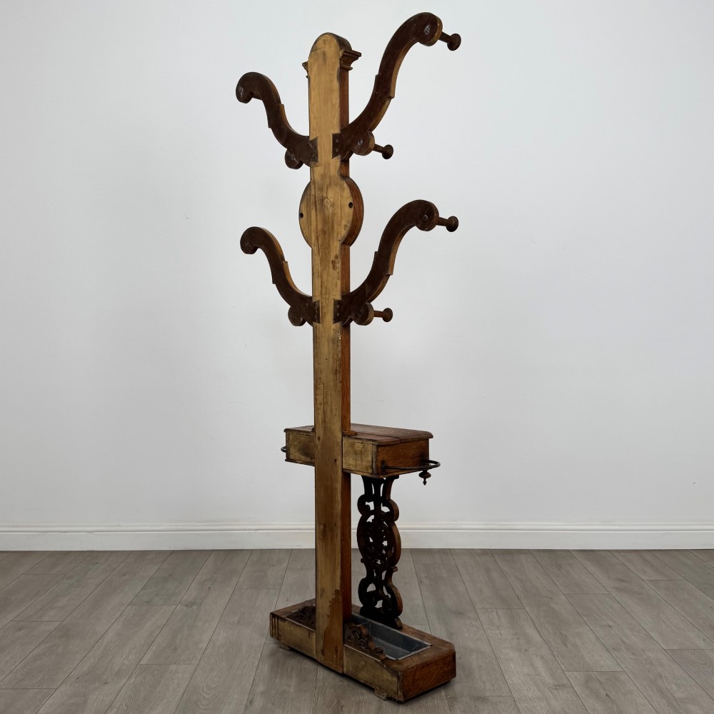A nineteenth-century Victorian mahogany hall stand featuring coat pegs, a central circular mirror, metal umbrella loops, carved lower scrollwork, and a base drip tray. View VI