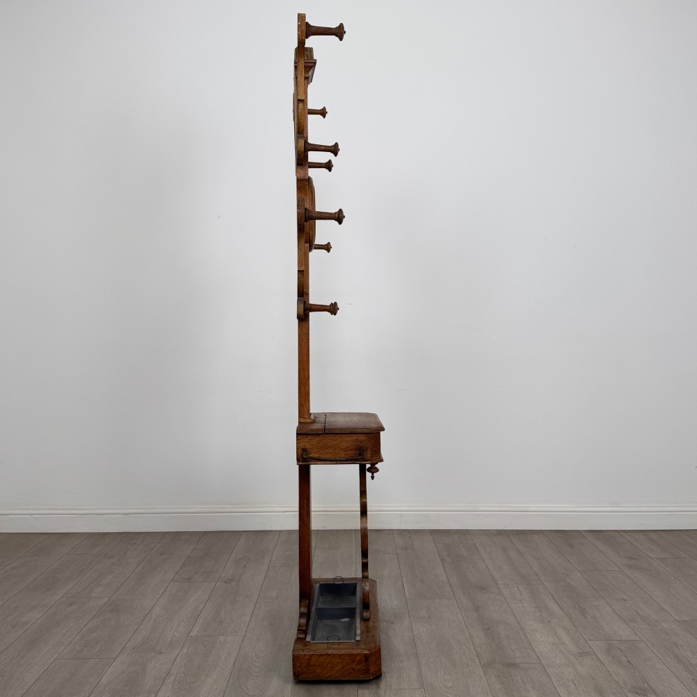A nineteenth-century Victorian mahogany hall stand featuring coat pegs, a central circular mirror, metal umbrella loops, carved lower scrollwork, and a base drip tray. View VII