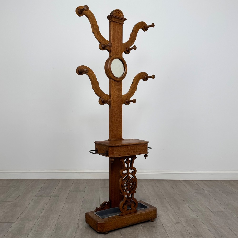 A nineteenth-century Victorian mahogany hall stand featuring coat pegs, a central circular mirror, metal umbrella loops, carved lower scrollwork, and a base drip tray. View VIII