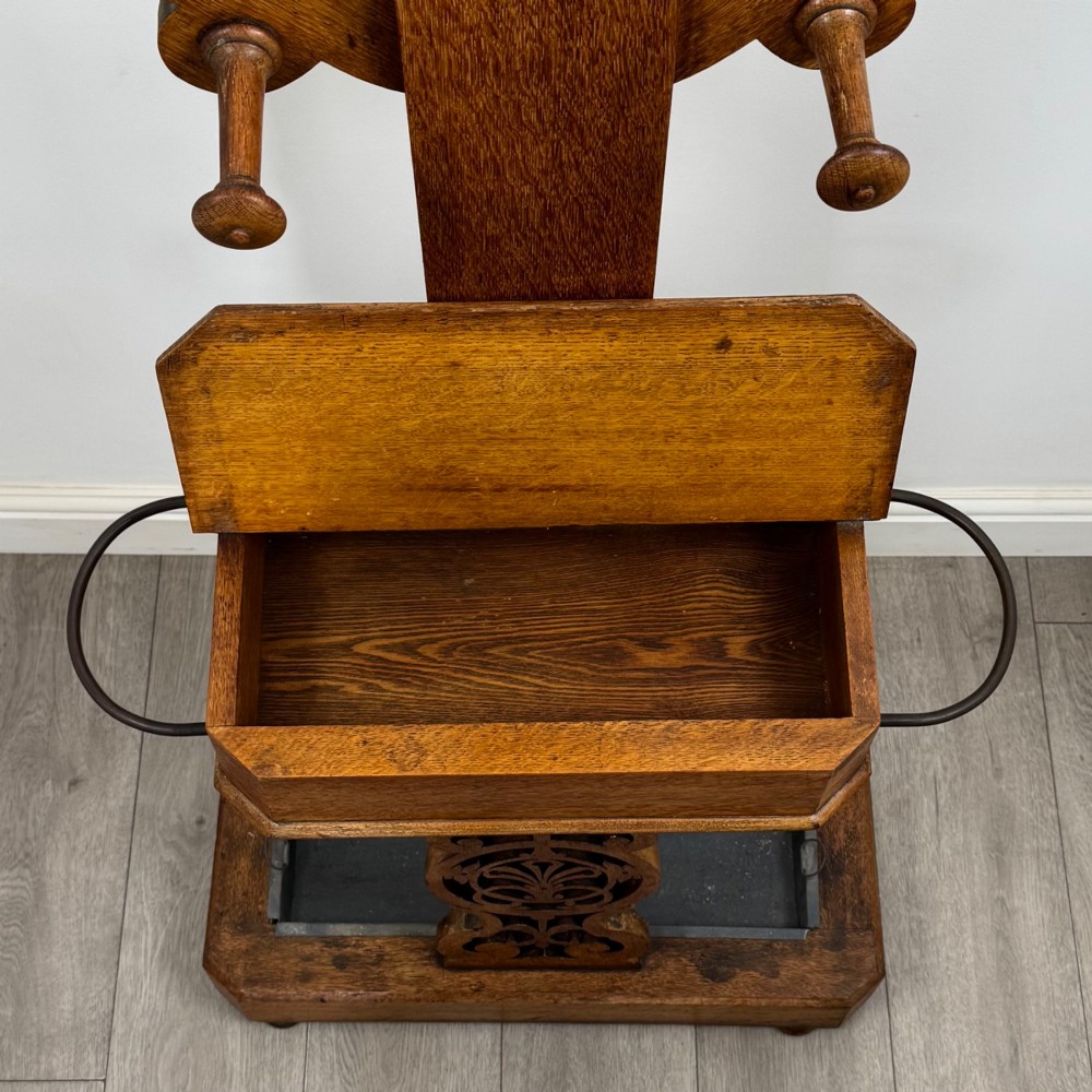 A nineteenth-century Victorian mahogany hall stand featuring coat pegs, a central circular mirror, metal umbrella loops, carved lower scrollwork, and a base drip tray. View X