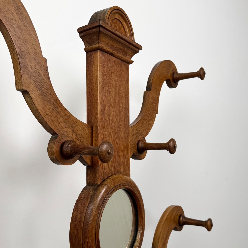 A nineteenth-century Victorian mahogany hall stand featuring coat pegs, a central circular mirror, metal umbrella loops, carved lower scrollwork, and a base drip tray. View XI