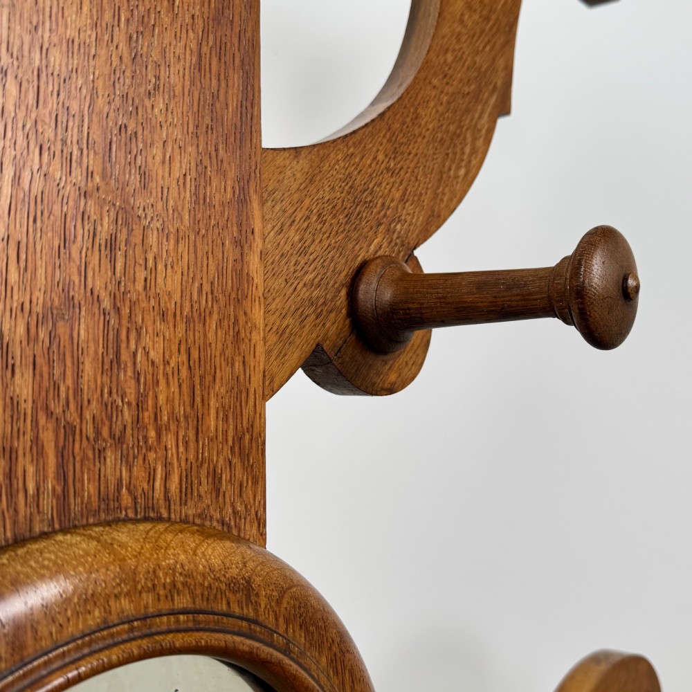 A nineteenth-century Victorian mahogany hall stand featuring coat pegs, a central circular mirror, metal umbrella loops, carved lower scrollwork, and a base drip tray. View XII