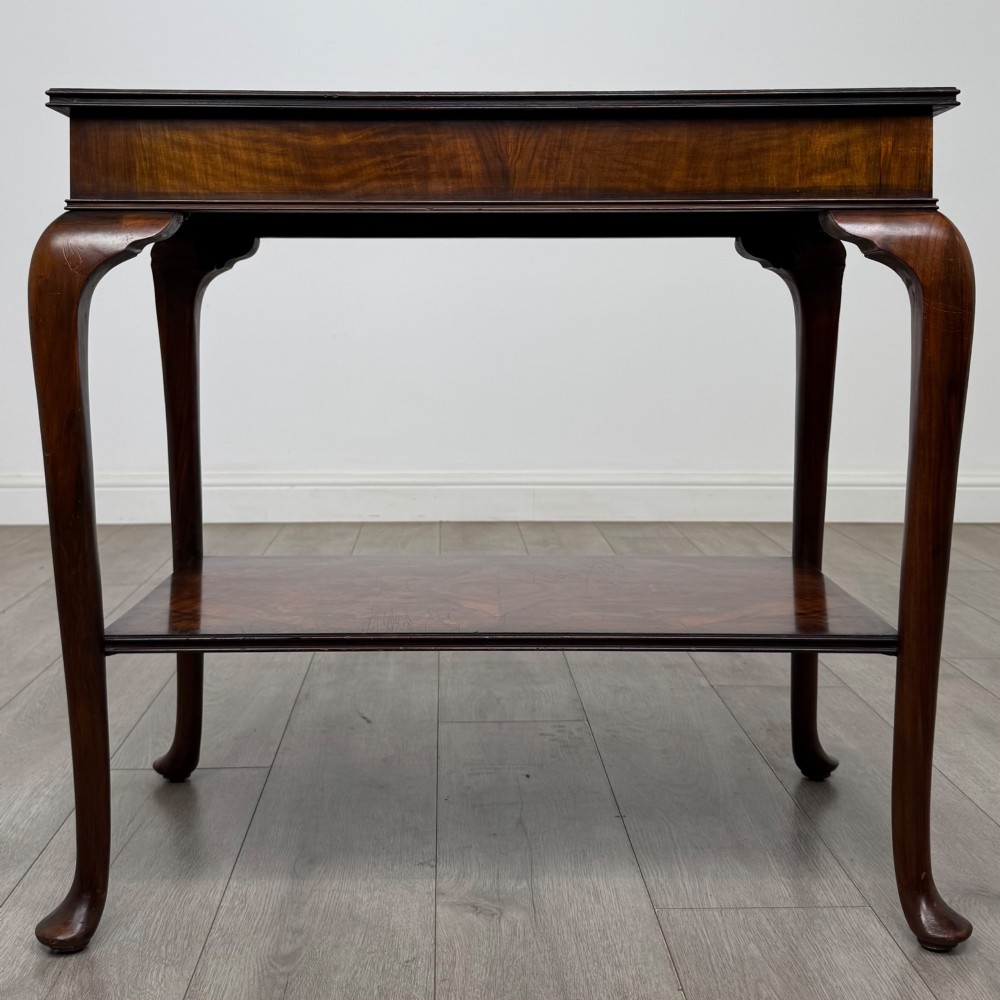 An Edwardian burr walnut side table featuring sloped cabriole legs, pad feet, a deep frieze, and a lower undertier shelf.