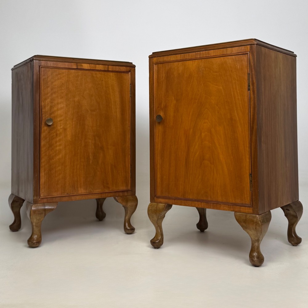 A pair of warm brown walnut bedside cabinets featuring single door cupboards, small round knobs, and carved cabriole legs with pad feet.