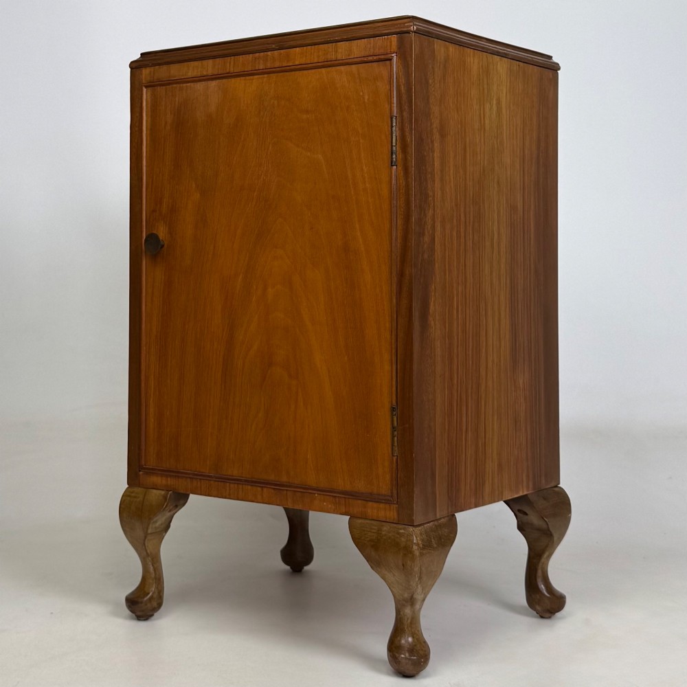 A pair of warm brown walnut bedside cabinets featuring single door cupboards, small round knobs, and carved cabriole legs with pad feet. View IV