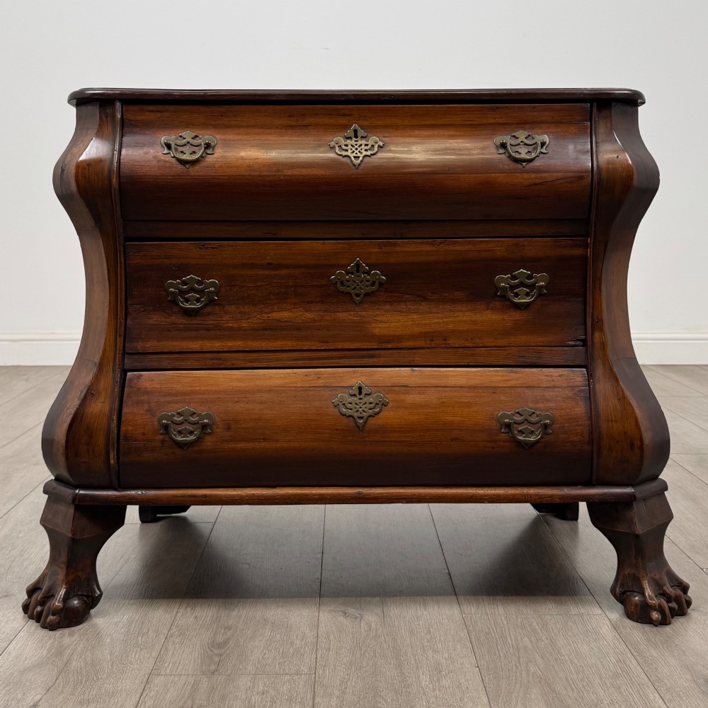 A small 20th-century Dutch bombe chest of drawers made from polished brown wood with three drawers, brass handles, and carved claw feet.