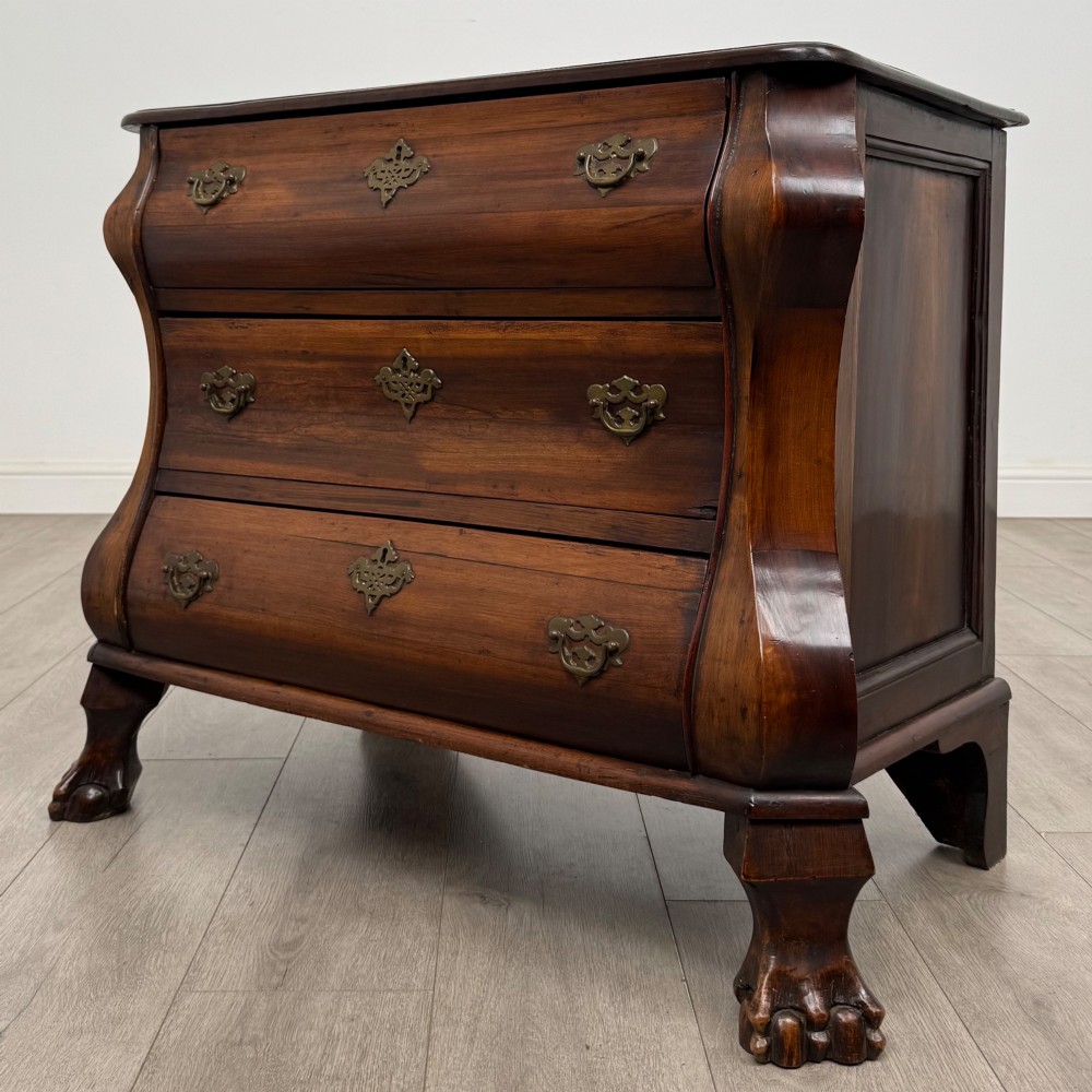 A small 20th-century Dutch bombe chest of drawers made from polished brown wood with three drawers, brass handles, and carved claw feet. View II