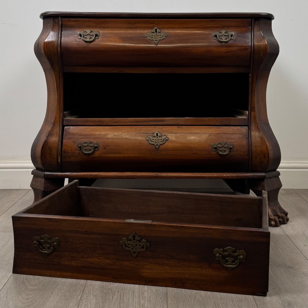 A small 20th-century Dutch bombe chest of drawers made from polished brown wood with three drawers, brass handles, and carved claw feet. View X