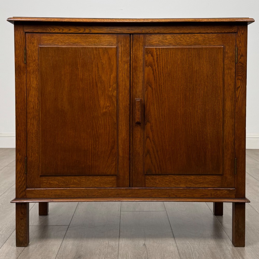 An Edwardian warm brown oak fitted cupboard featuring twin recessed panel doors, a central wooden latch, and four straight legs.