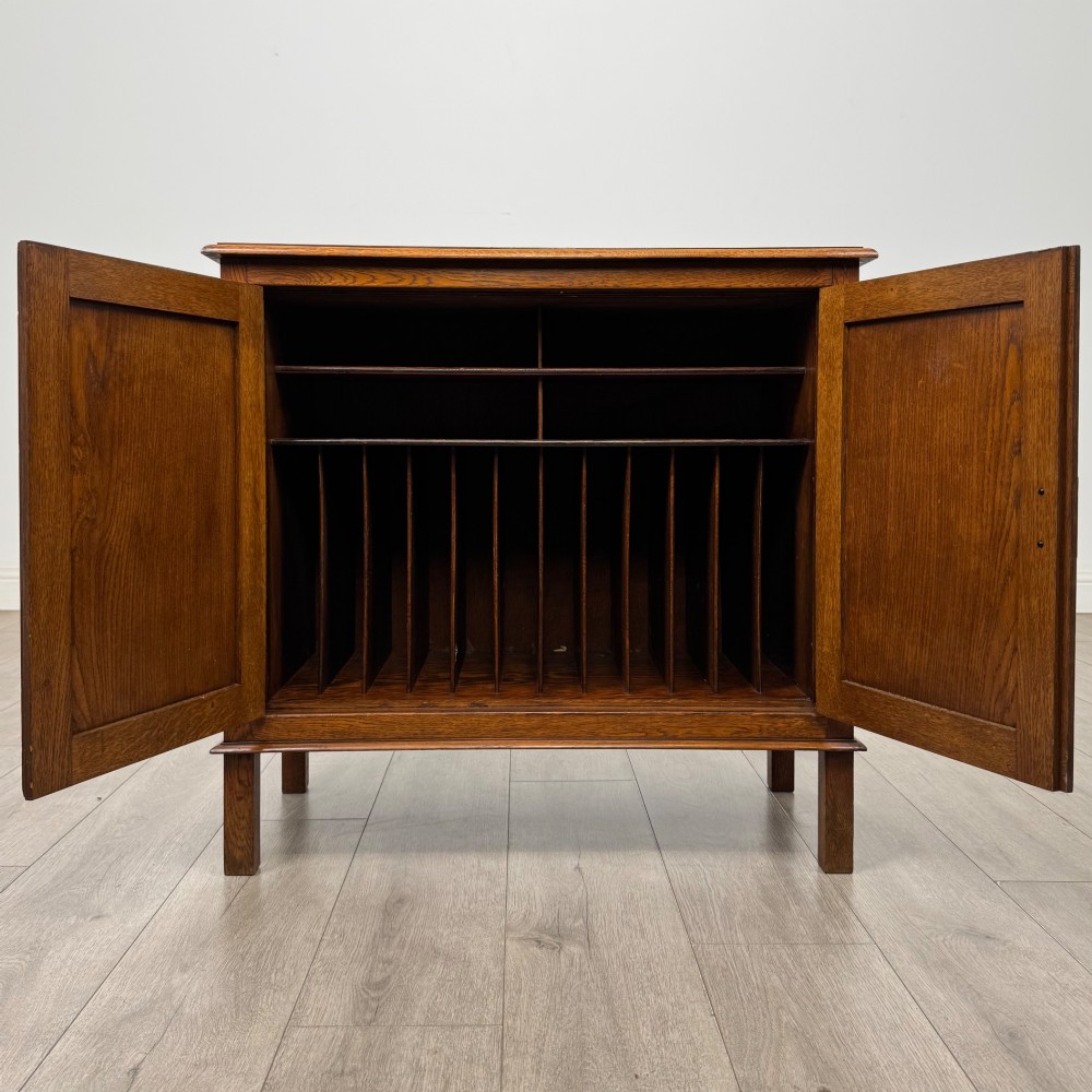 An Edwardian warm brown oak fitted cupboard featuring twin recessed panel doors, a central wooden latch, and four straight legs. View II