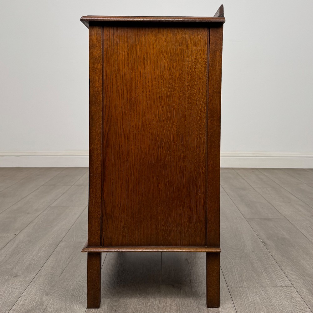 An Edwardian warm brown oak fitted cupboard featuring twin recessed panel doors, a central wooden latch, and four straight legs. View IV