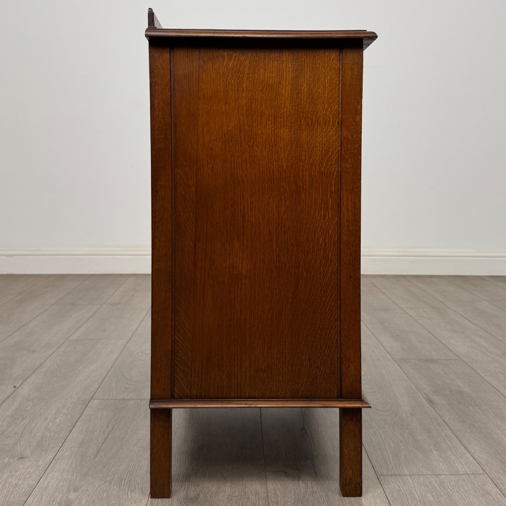 An Edwardian warm brown oak fitted cupboard featuring twin recessed panel doors, a central wooden latch, and four straight legs. View VIII