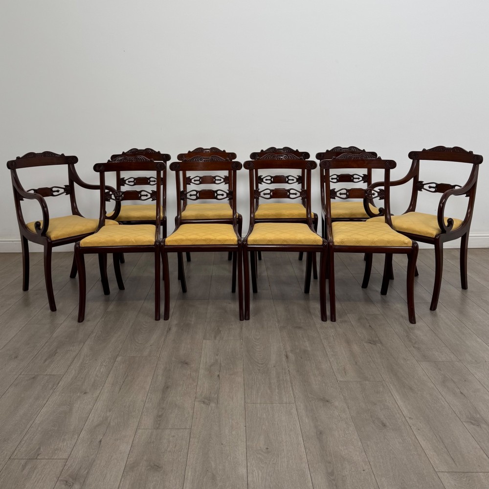 A set of ten mahogany Regency style dining chairs with yellow upholstered seats, including eight side chairs and two carvers with scrolling arms.