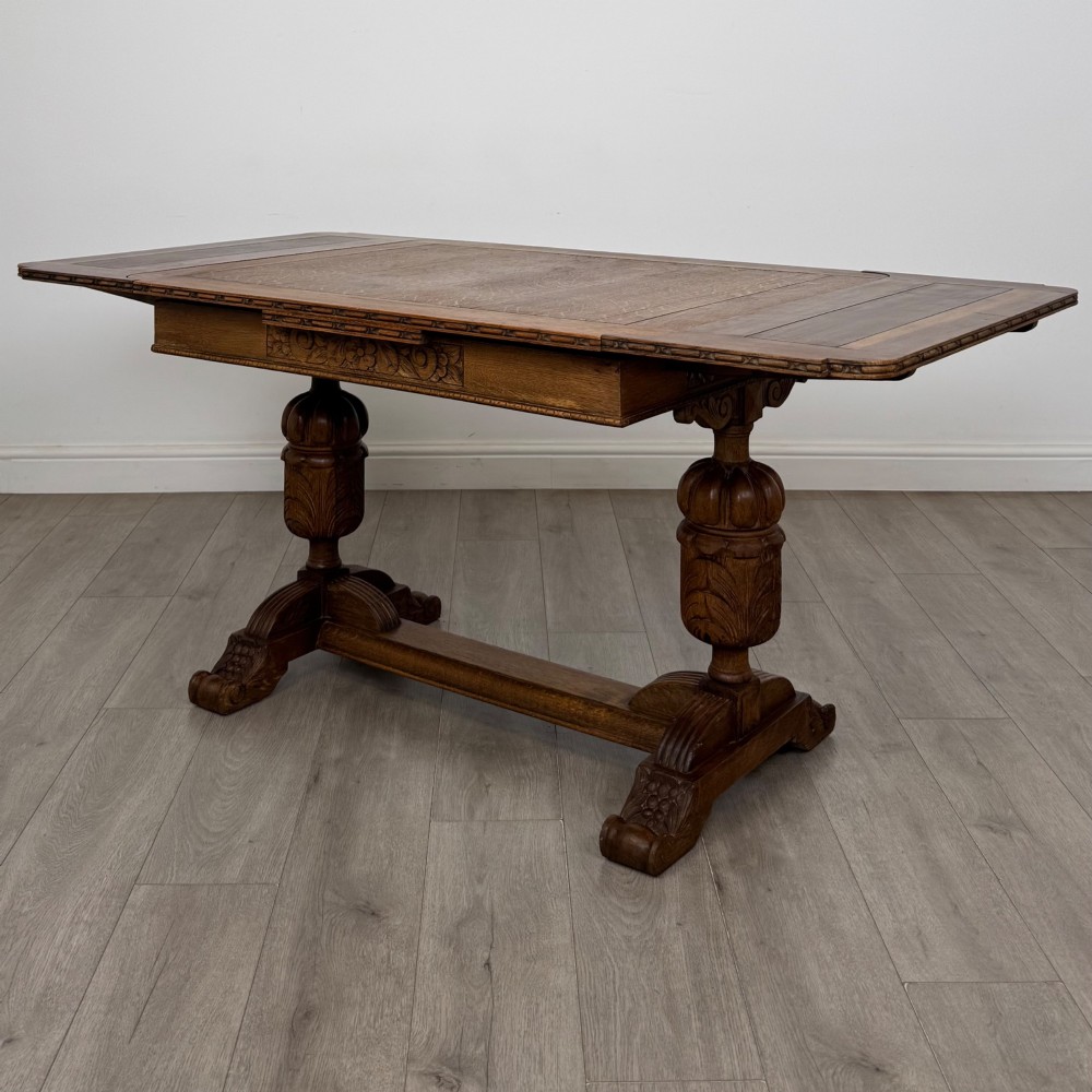 An antique Edwardian oak draw-leaf dining table featuring carved bulbous supports and a central stretcher.