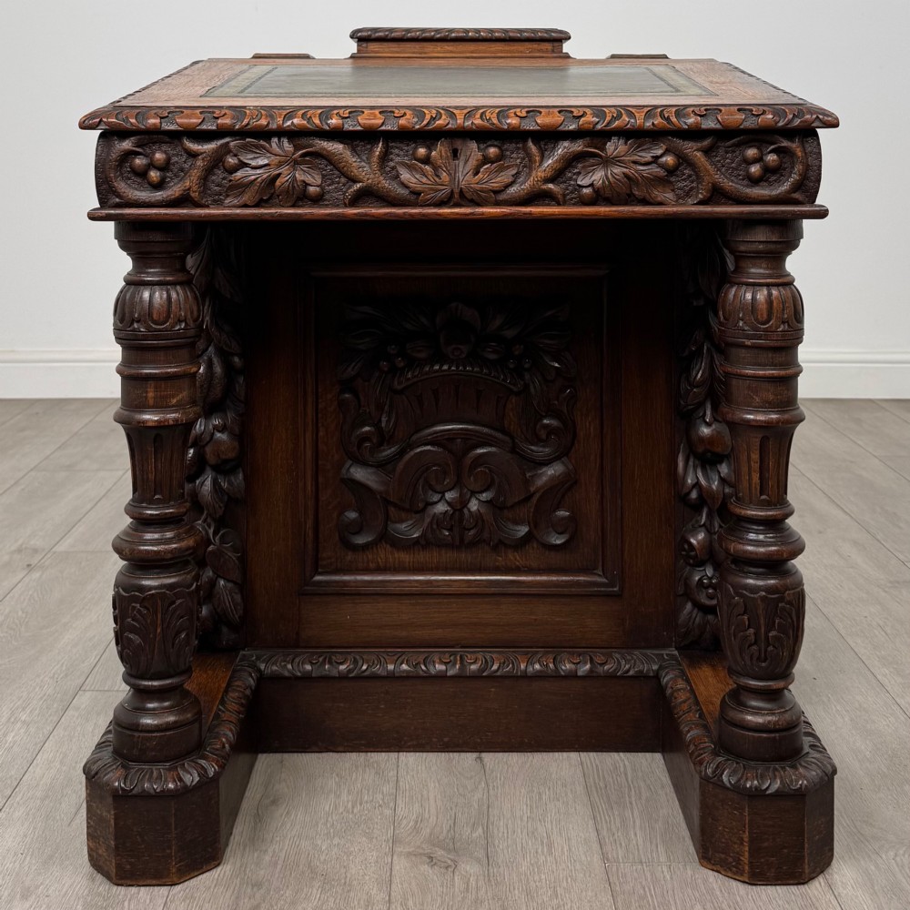 A 19th-century Victorian carved oak davenport desk featuring heavy foliate carvings, turned columns, and a green leather insert.
