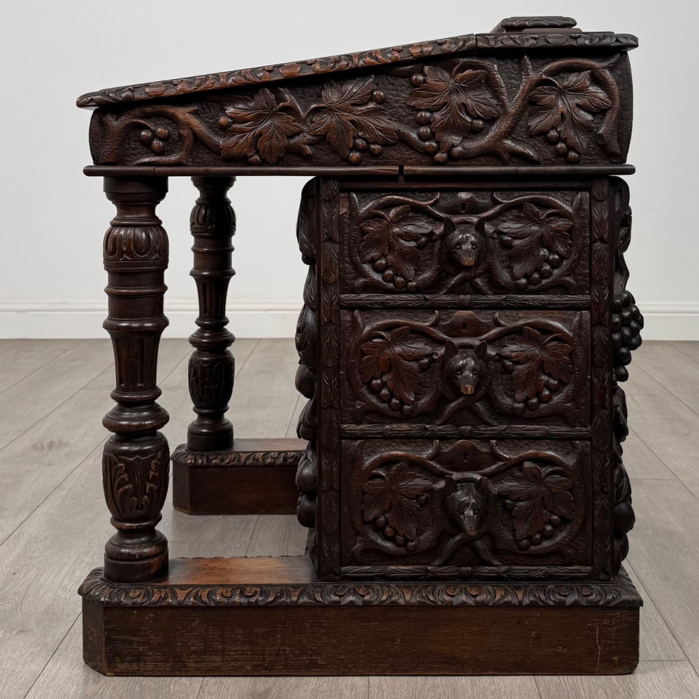 A 19th-century Victorian carved oak davenport desk featuring heavy foliate carvings, turned columns, and a green leather insert. View III
