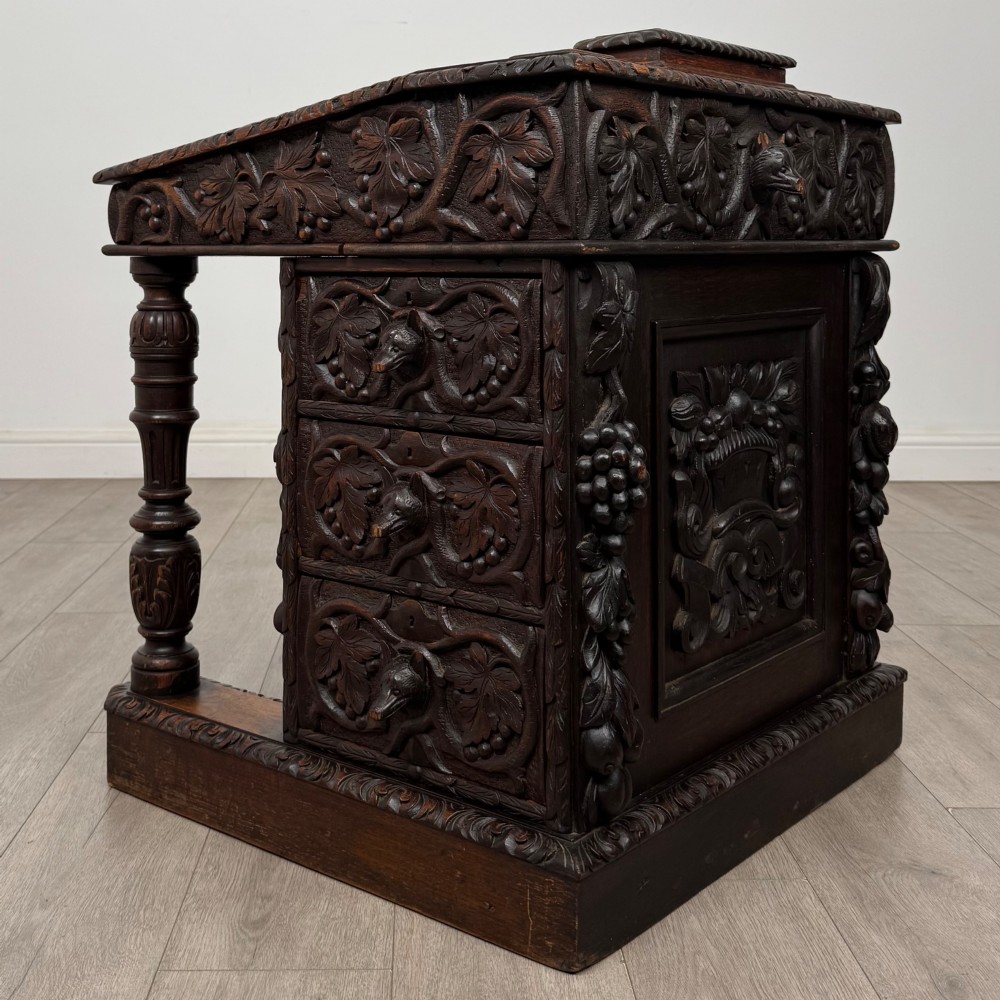 A 19th-century Victorian carved oak davenport desk featuring heavy foliate carvings, turned columns, and a green leather insert. View IV