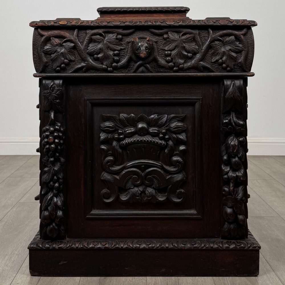 A 19th-century Victorian carved oak davenport desk featuring heavy foliate carvings, turned columns, and a green leather insert. View V