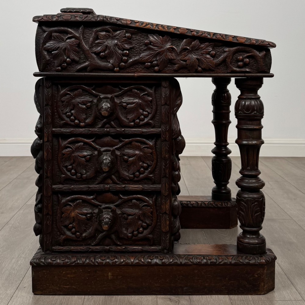 A 19th-century Victorian carved oak davenport desk featuring heavy foliate carvings, turned columns, and a green leather insert. View VII