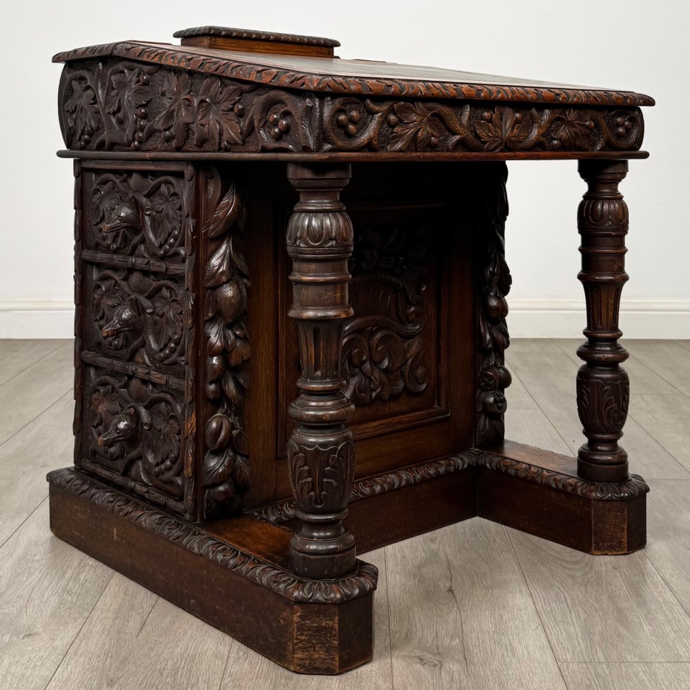A 19th-century Victorian carved oak davenport desk featuring heavy foliate carvings, turned columns, and a green leather insert. View VIII