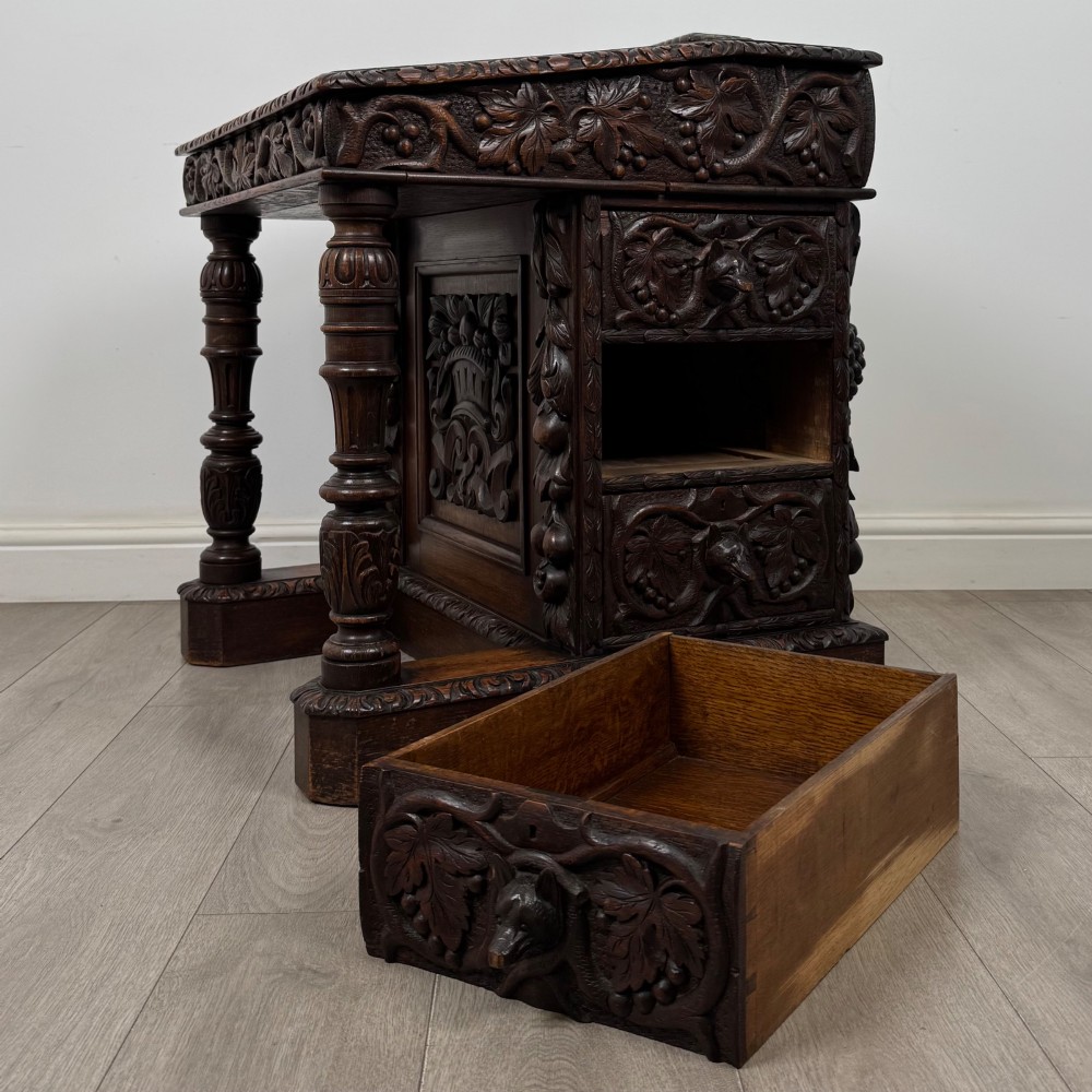 A 19th-century Victorian carved oak davenport desk featuring heavy foliate carvings, turned columns, and a green leather insert. View XI