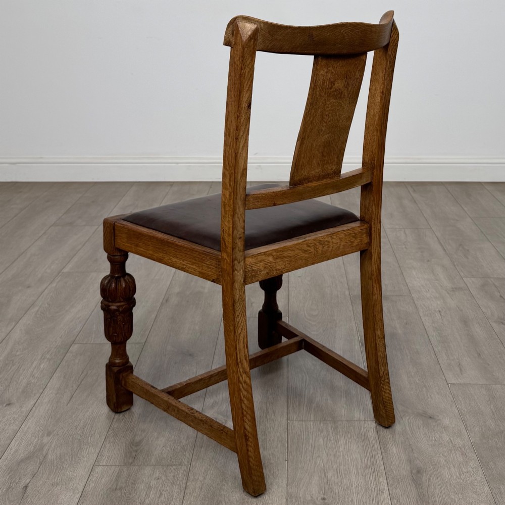 A set of four Edwardian oak dining chairs featuring carved back splats, brown upholstered seats, and bulbous turned front legs. View III