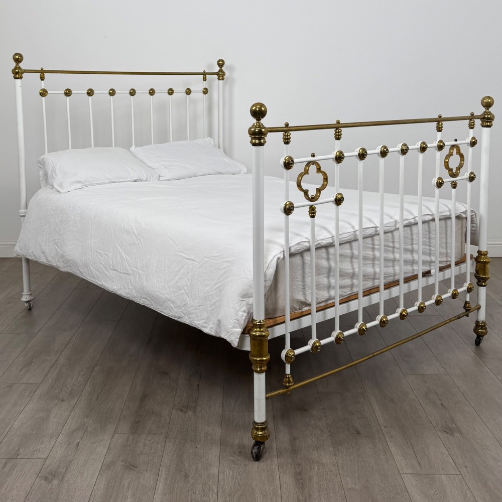 Victorian white-painted iron and polished brass king-size bedstead featuring round brass finials and quatrefoil metalwork.