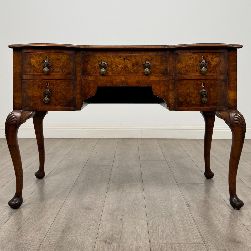 An Edwardian burr walnut writing table featuring five drawers with brass drop handles and carved cabriole legs.
