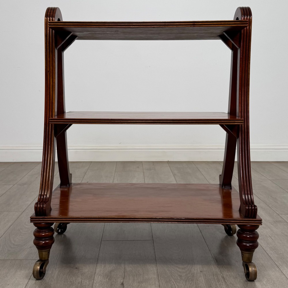 A three-tiered mahogany trolley featuring arched reeded side supports and turned feet resting on brass castors. View IV