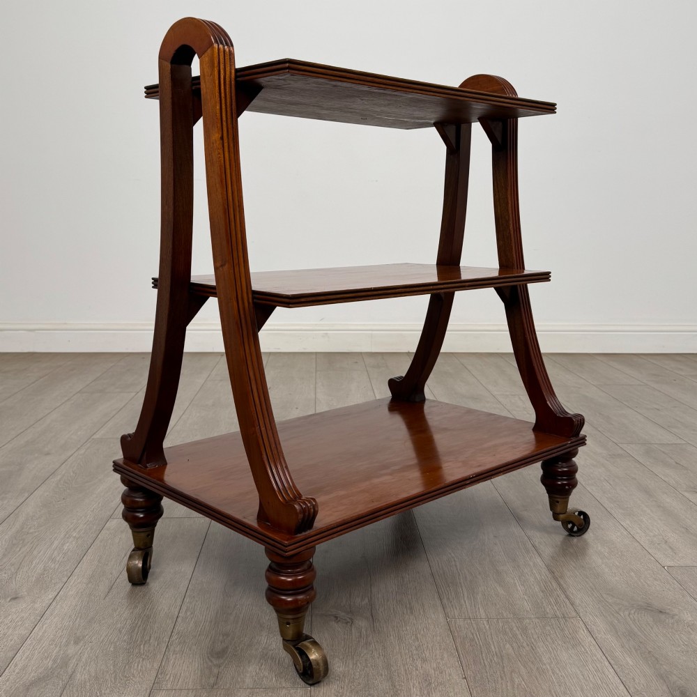 A three-tiered mahogany trolley featuring arched reeded side supports and turned feet resting on brass castors. View VII