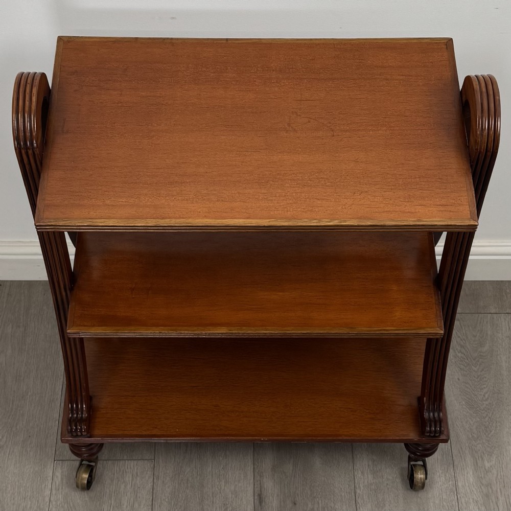 A three-tiered mahogany trolley featuring arched reeded side supports and turned feet resting on brass castors. View VIII