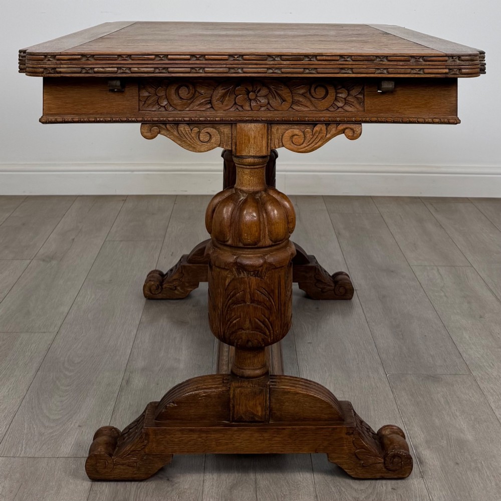 An early twentieth-century oak dining table featuring carved frieze detailing and heavy turned legs, shown alongside four matching oak dining chairs with dark leather seats. View XI