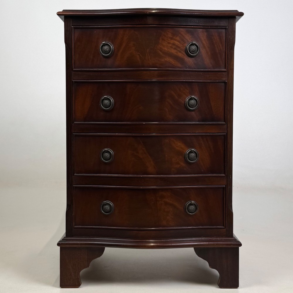 A small mahogany chest of four drawers featuring flame grain veneer fronts, circular brass ring handles, and bracket feet.