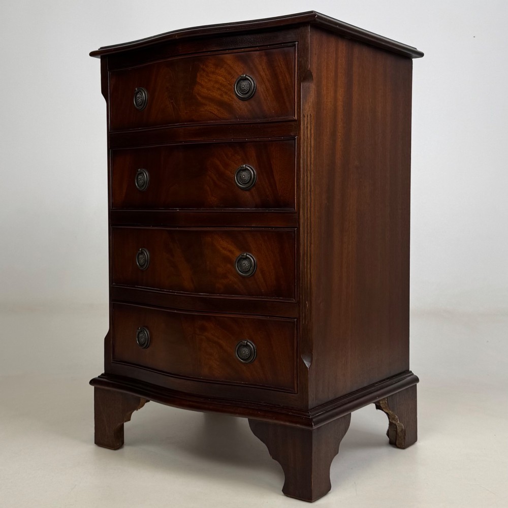 A small mahogany chest of four drawers featuring flame grain veneer fronts, circular brass ring handles, and bracket feet. View II