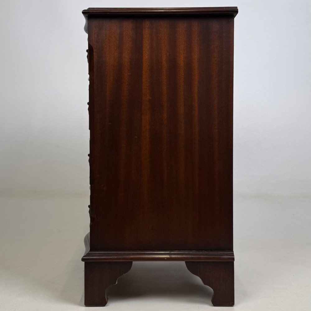 A small mahogany chest of four drawers featuring flame grain veneer fronts, circular brass ring handles, and bracket feet. View III