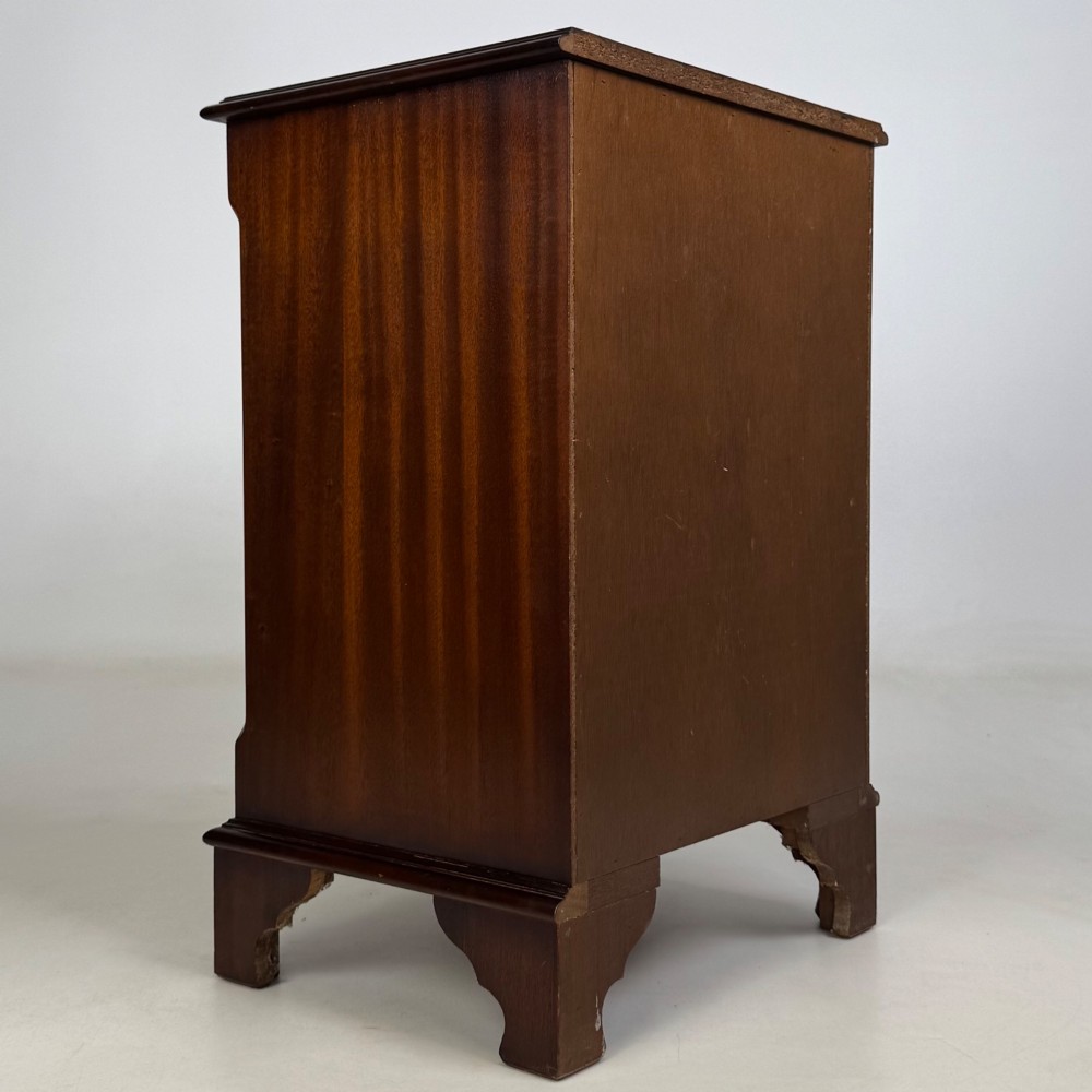 A small mahogany chest of four drawers featuring flame grain veneer fronts, circular brass ring handles, and bracket feet. View IV