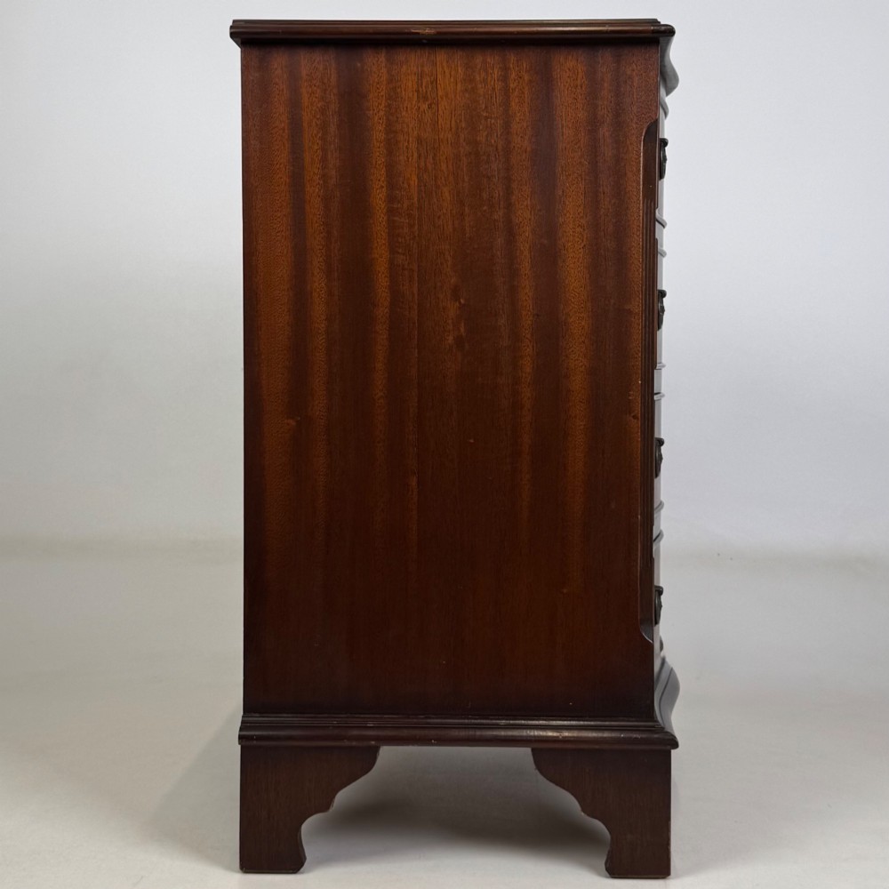 A small mahogany chest of four drawers featuring flame grain veneer fronts, circular brass ring handles, and bracket feet. View VII