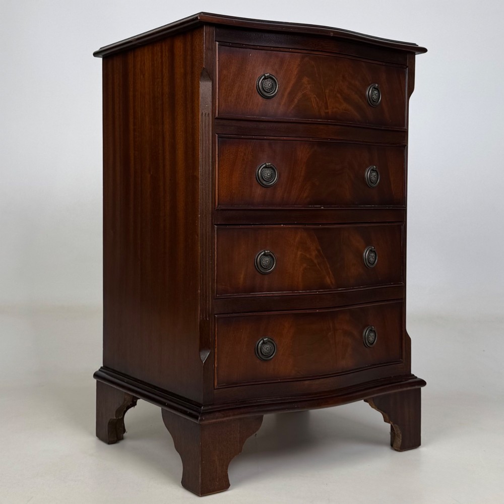A small mahogany chest of four drawers featuring flame grain veneer fronts, circular brass ring handles, and bracket feet. View VIII
