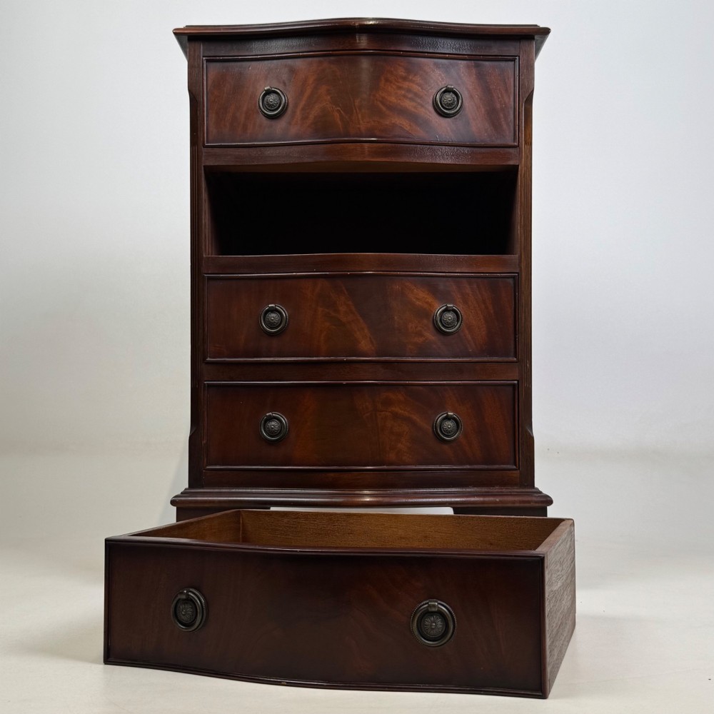 A small mahogany chest of four drawers featuring flame grain veneer fronts, circular brass ring handles, and bracket feet. View IX