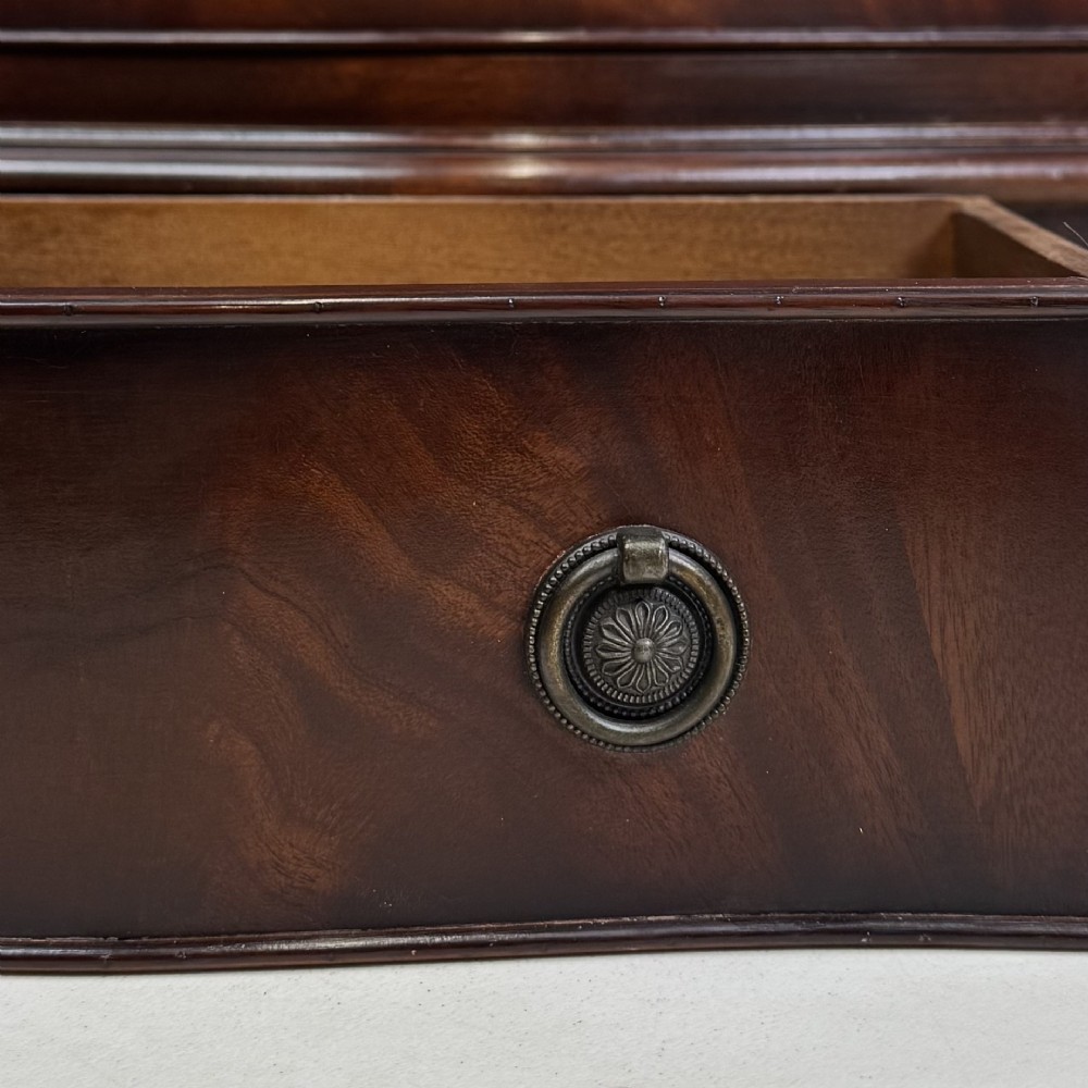 A small mahogany chest of four drawers featuring flame grain veneer fronts, circular brass ring handles, and bracket feet. View X