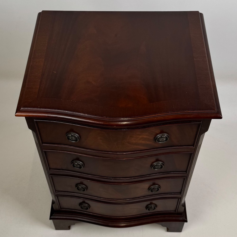 A small mahogany chest of four drawers featuring flame grain veneer fronts, circular brass ring handles, and bracket feet. View XI