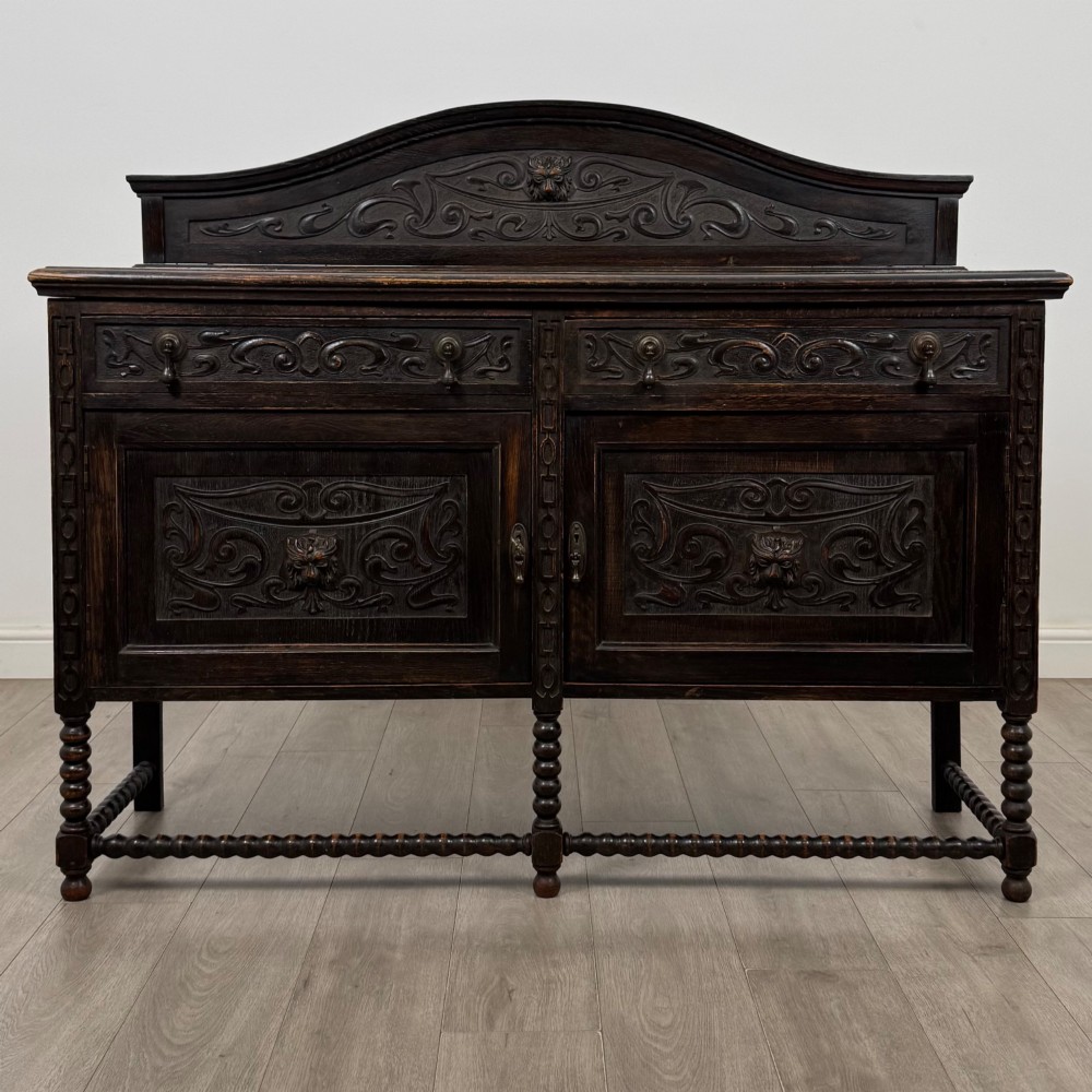 A dark oak 19th-century sideboard featuring carved lion mask motifs, scrollwork panel doors, and bobbin-turned legs connected by stretchers.