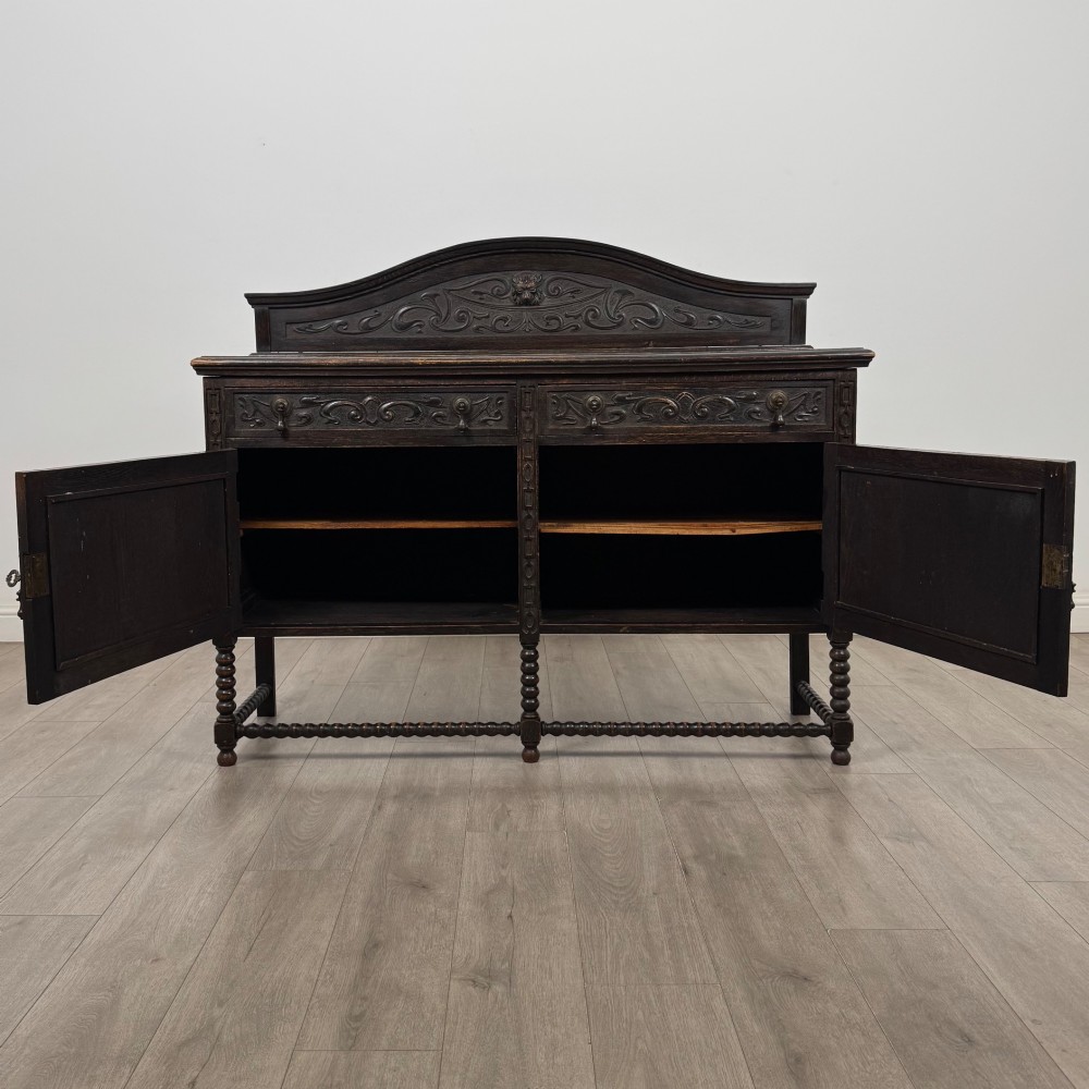 A dark oak 19th-century sideboard featuring carved lion mask motifs, scrollwork panel doors, and bobbin-turned legs connected by stretchers. View II