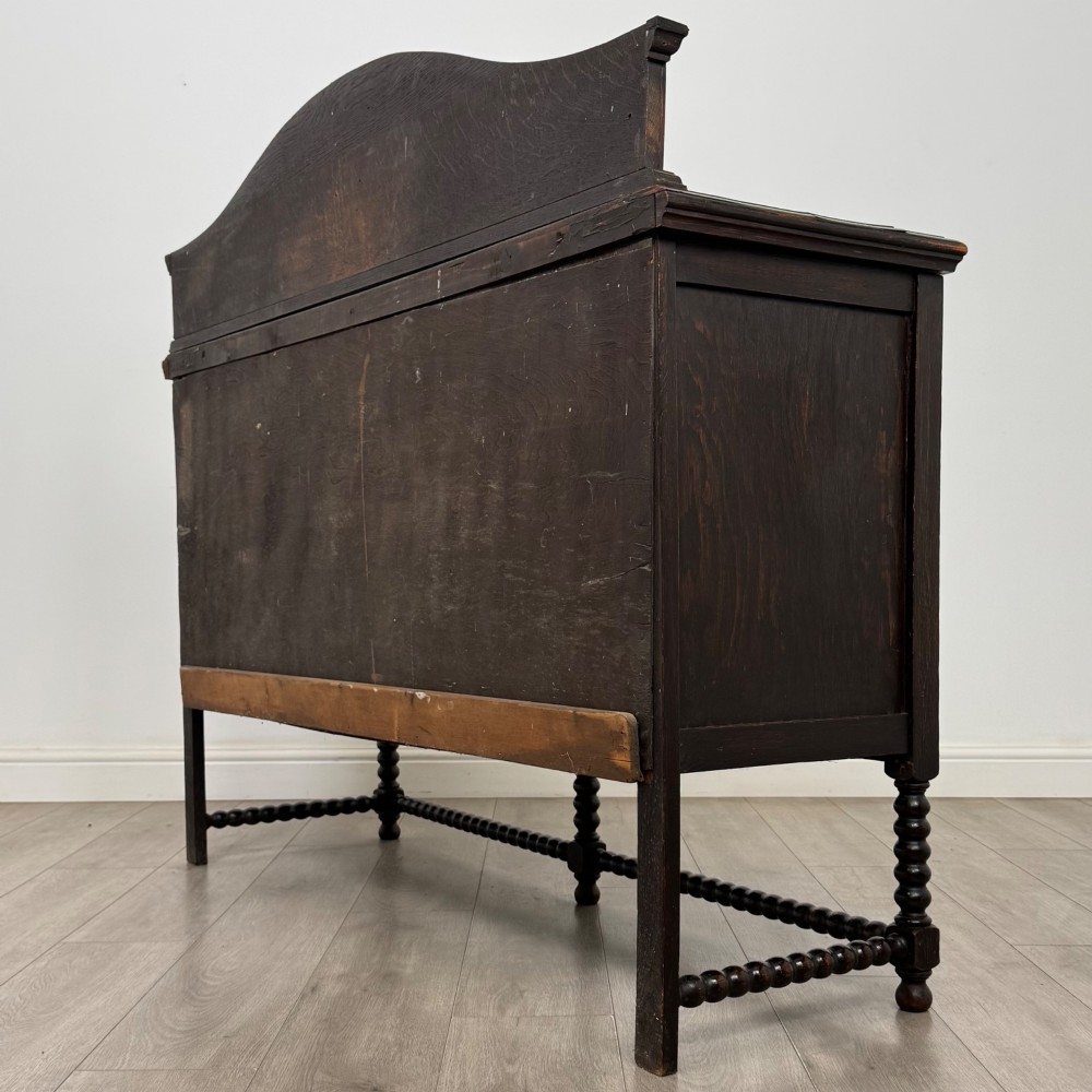 A dark oak 19th-century sideboard featuring carved lion mask motifs, scrollwork panel doors, and bobbin-turned legs connected by stretchers. View VII